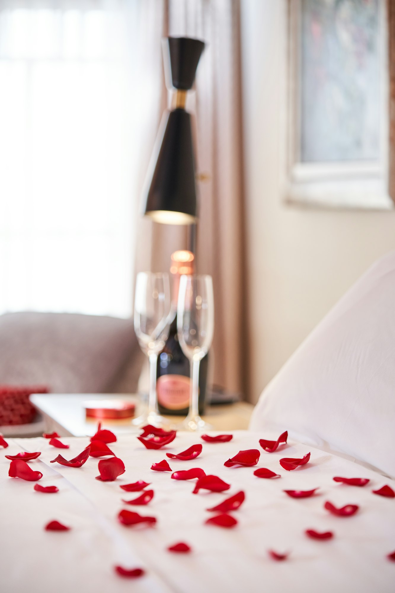 Bed covered with rose petals and bottle of champagne